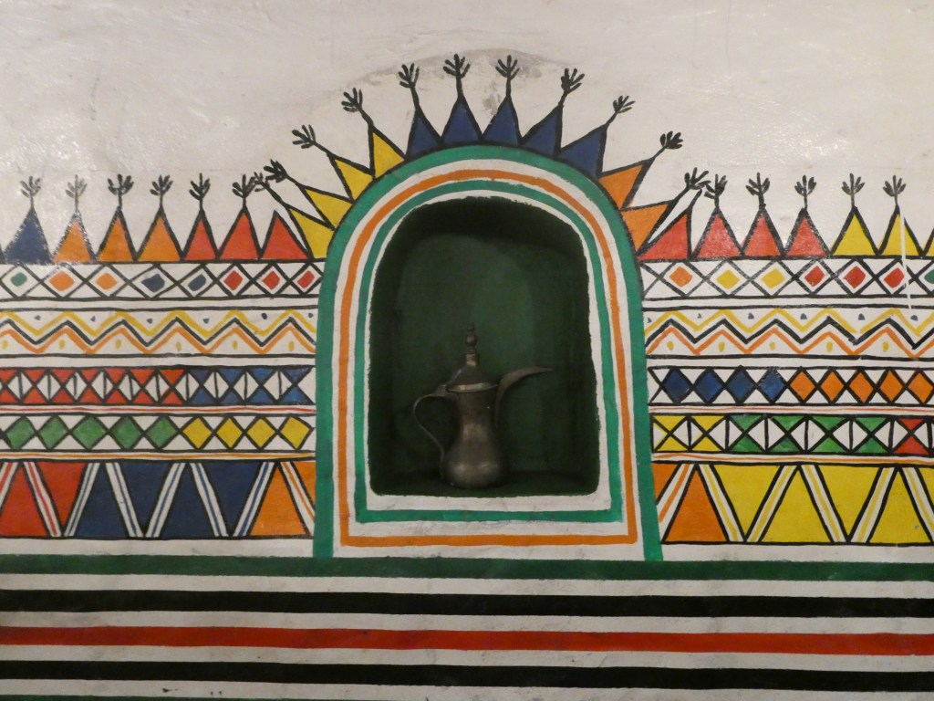 Une niche décorée de motifs colorés avec une théière traditionnelle en métal au centre.