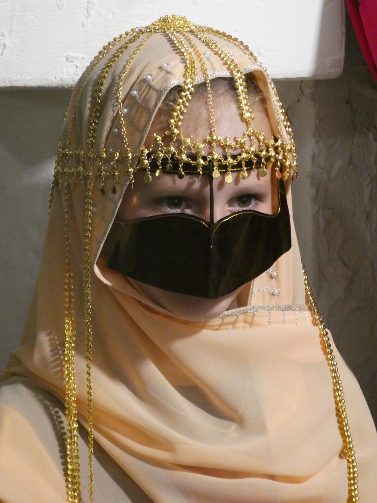 Femme portant un hijab traditionnel orné de bijoux et un voile couvrant partiellement le visage.