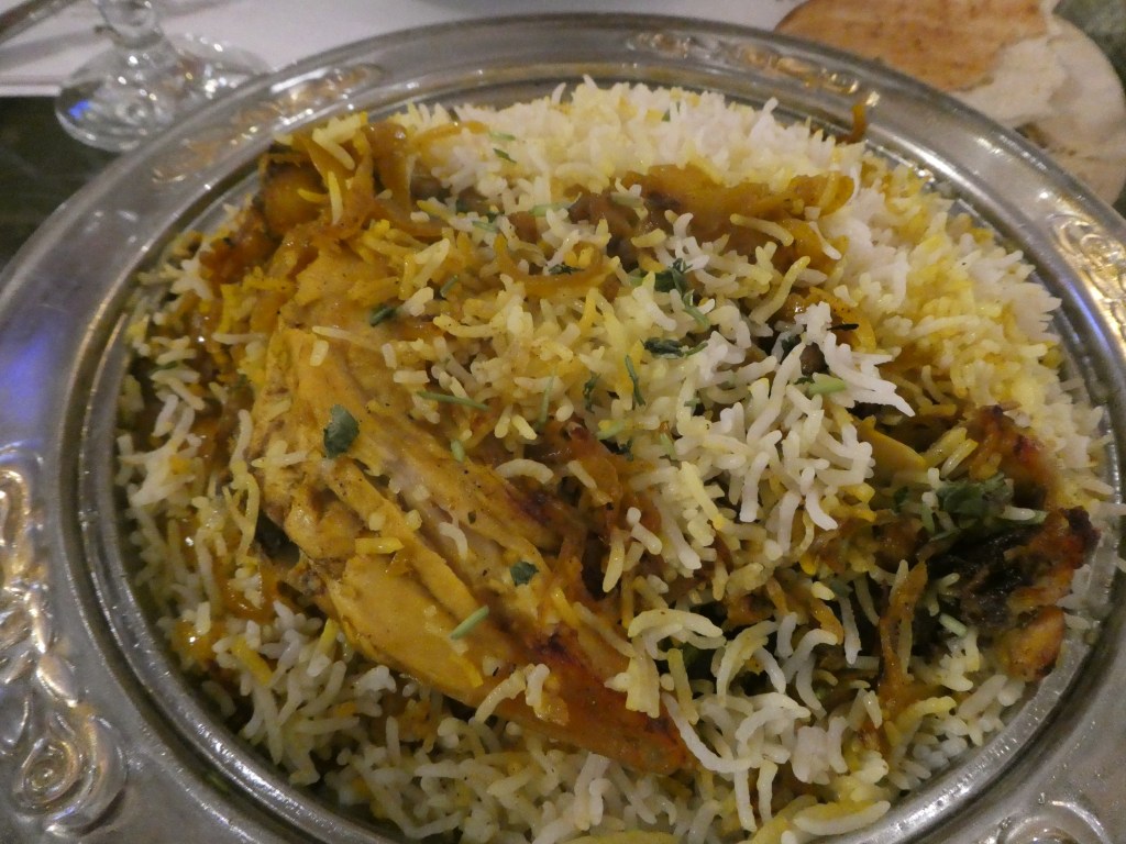 Un plat traditionnel saoudien de riz basmati aromatisé et de poulet grillé, servi dans un plat en métal, accompagné de pain à côté.