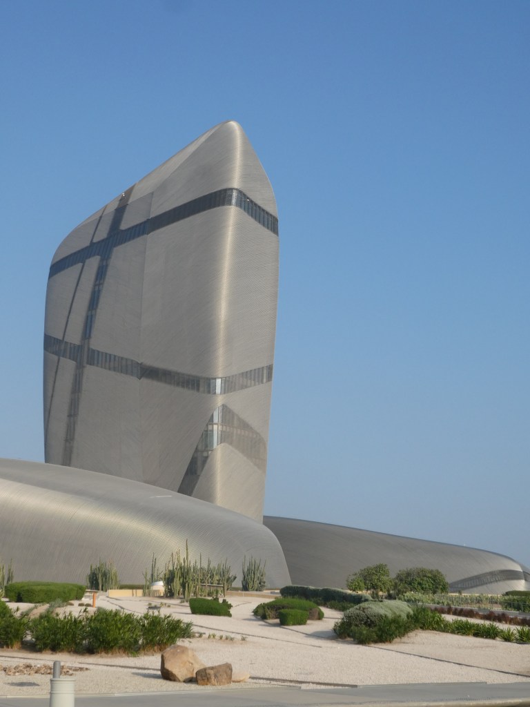 Vue du centre du roi Abdulaziz pour la connaissance et la culture, un bâtiment moderne aux formes uniques et au design futuriste, entouré de jardins soignés sous un ciel bleu.