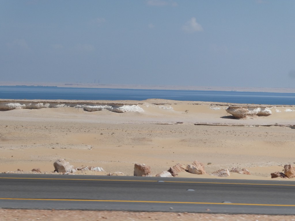 Vue d'un paysage désertique en Arabie Saoudite avec une étendue de sable et la mer en arrière-plan.