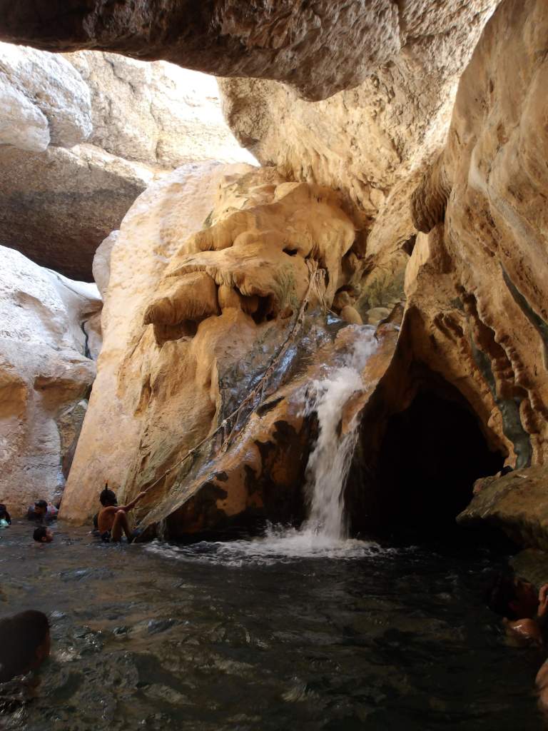 Un groupe de personnes se baignant dans une piscine naturelle, avec une cascade se déversant sur des rochers dans un environnement rocheux.