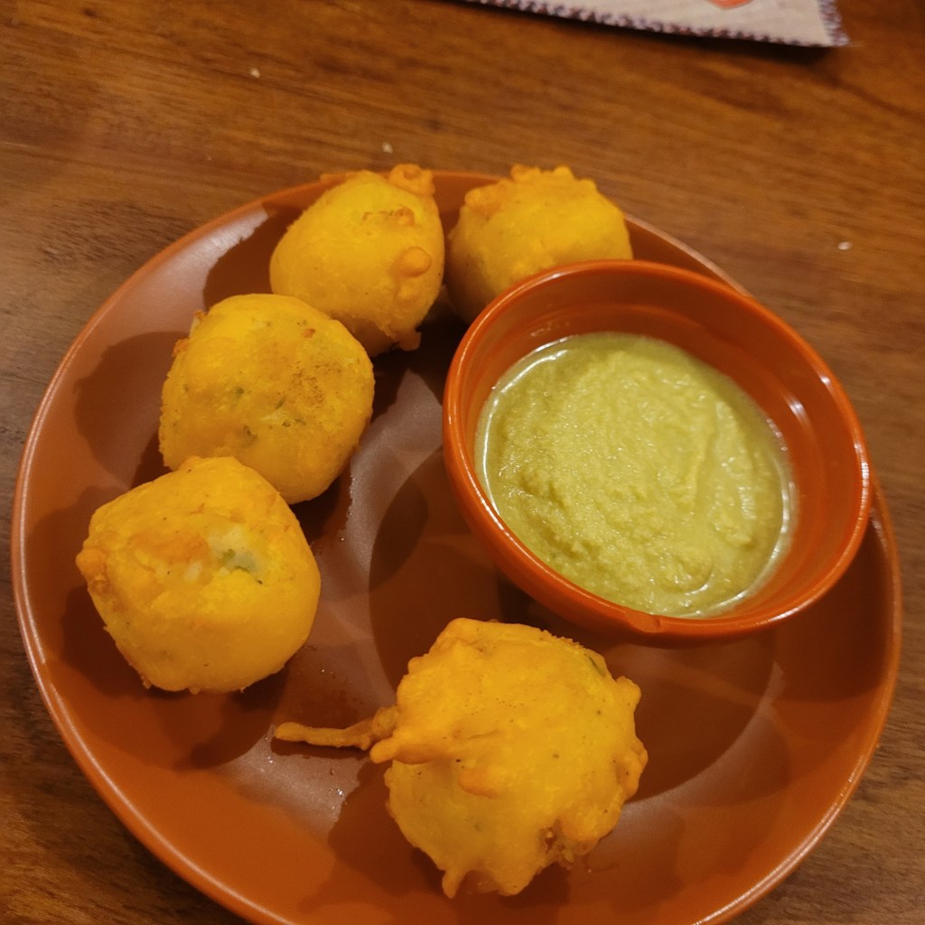 Une assiette de cinq boules frites dorées accompagnées d'une petite coupelle de sauce verte.