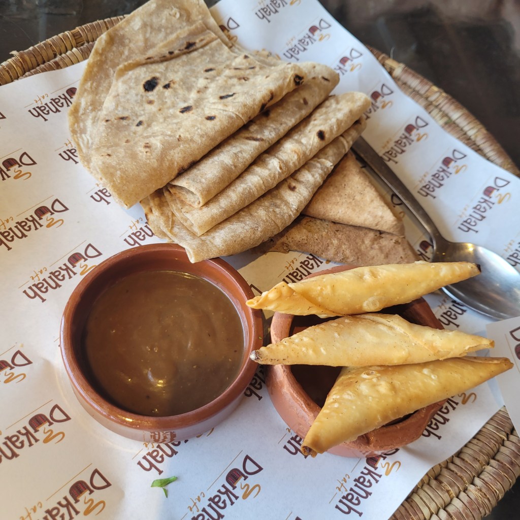Assiette de pains plats avec un bol de sauce et des samoussas, présentée sur un fond de papier à motif.