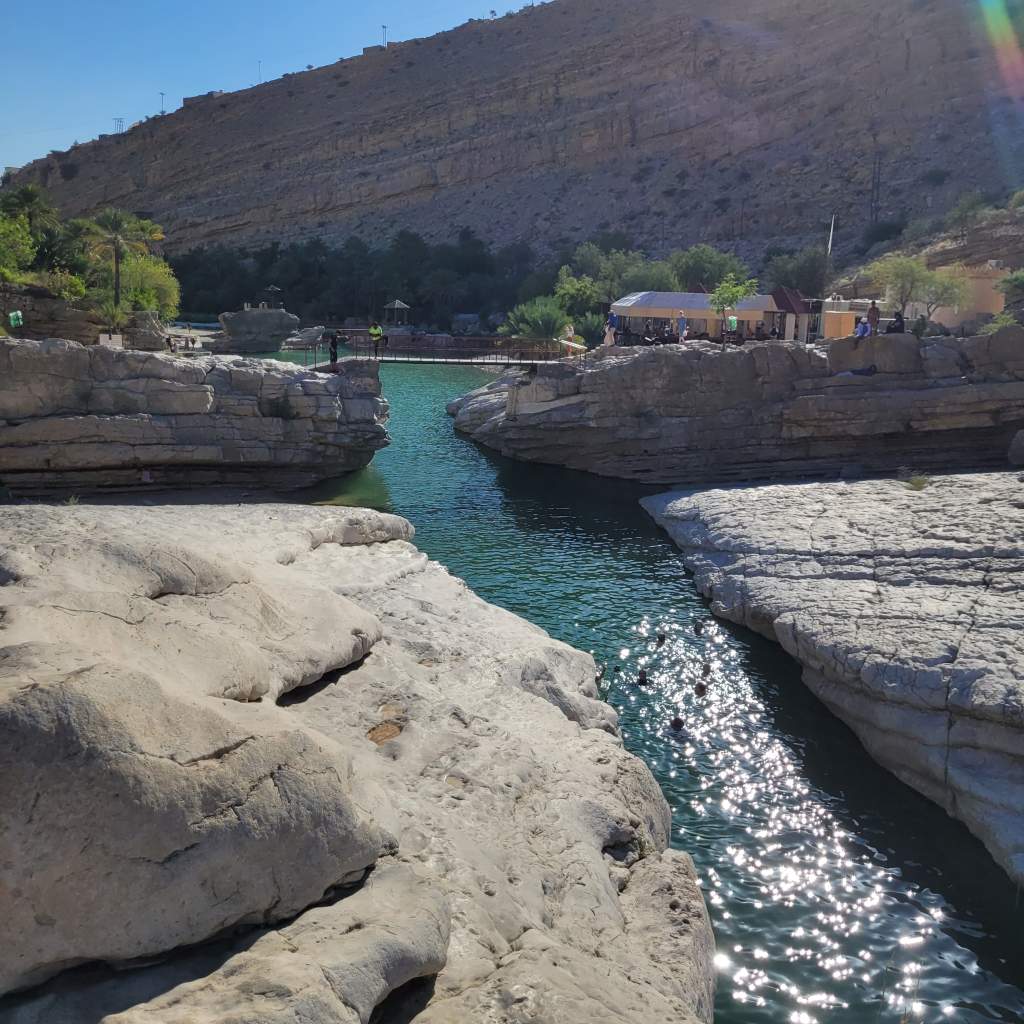 Vue d'un paysage naturel avec des rochers et une eau claire entre deux formations rocheuses, sous un ciel ensoleillé.