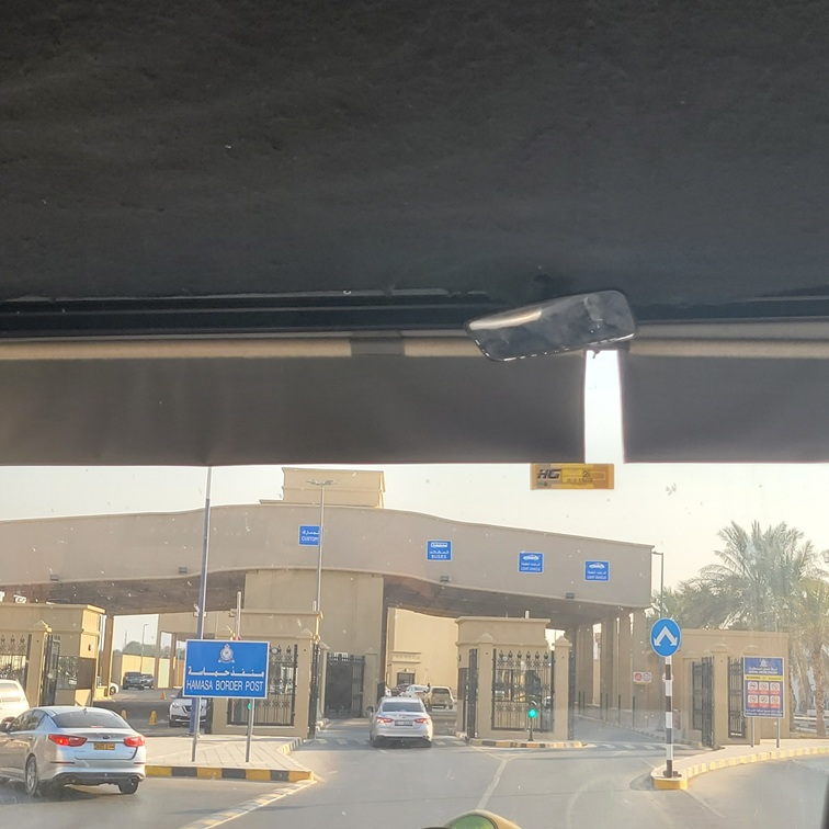 Poste frontière de Hamsa, vue depuis un véhicule, avec des panneaux de signalisation et des voitures en attente.