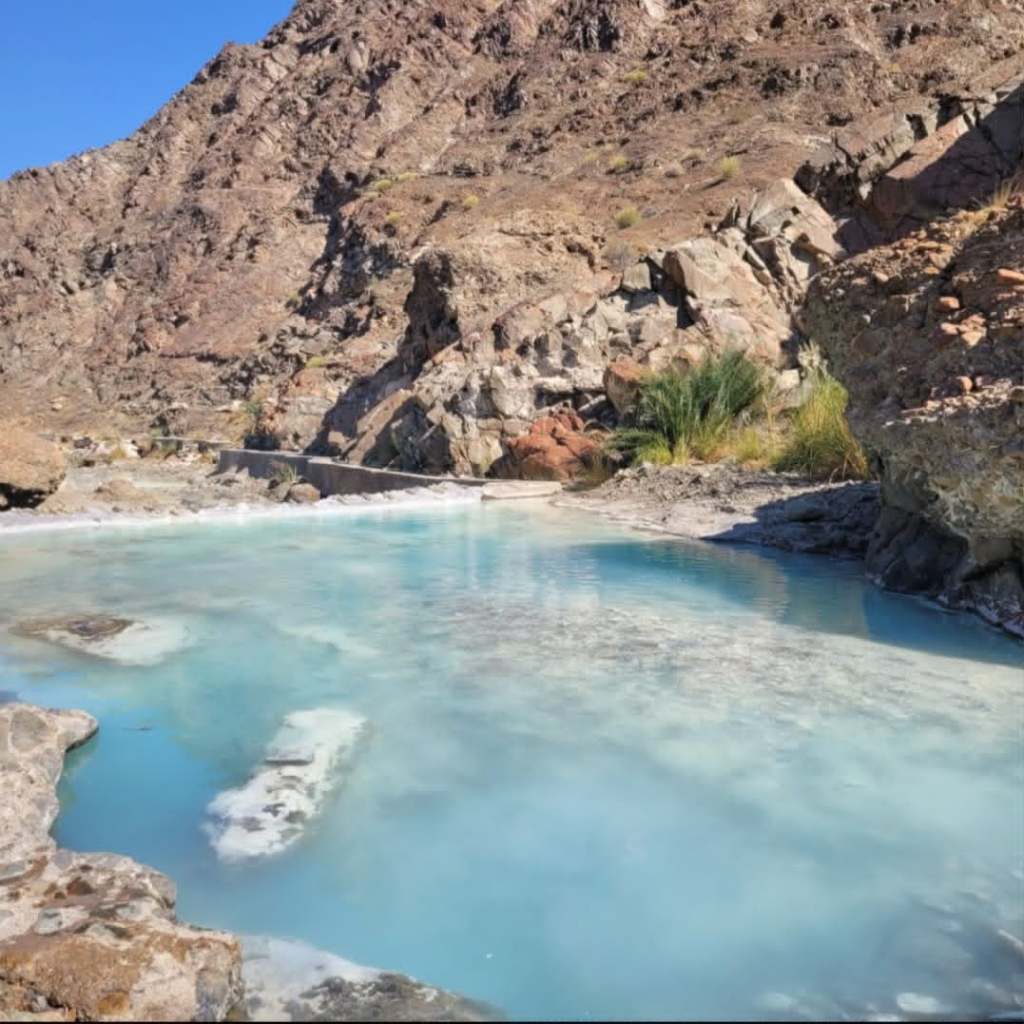 Une source d'eau claire et turquoise au milieu de rochers arides sous un ciel bleu.