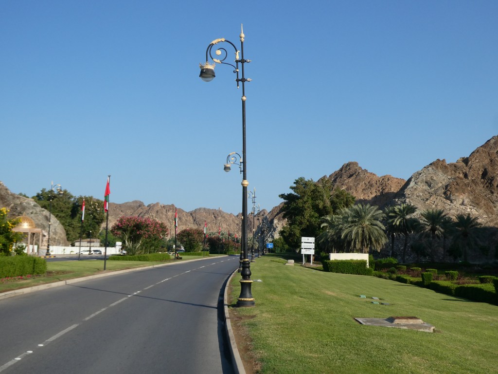 Une vue d'une route bordée de lampadaires, avec des montagnes en arrière-plan et des drapeaux décorant le bord de la route, sous un ciel bleu clair.