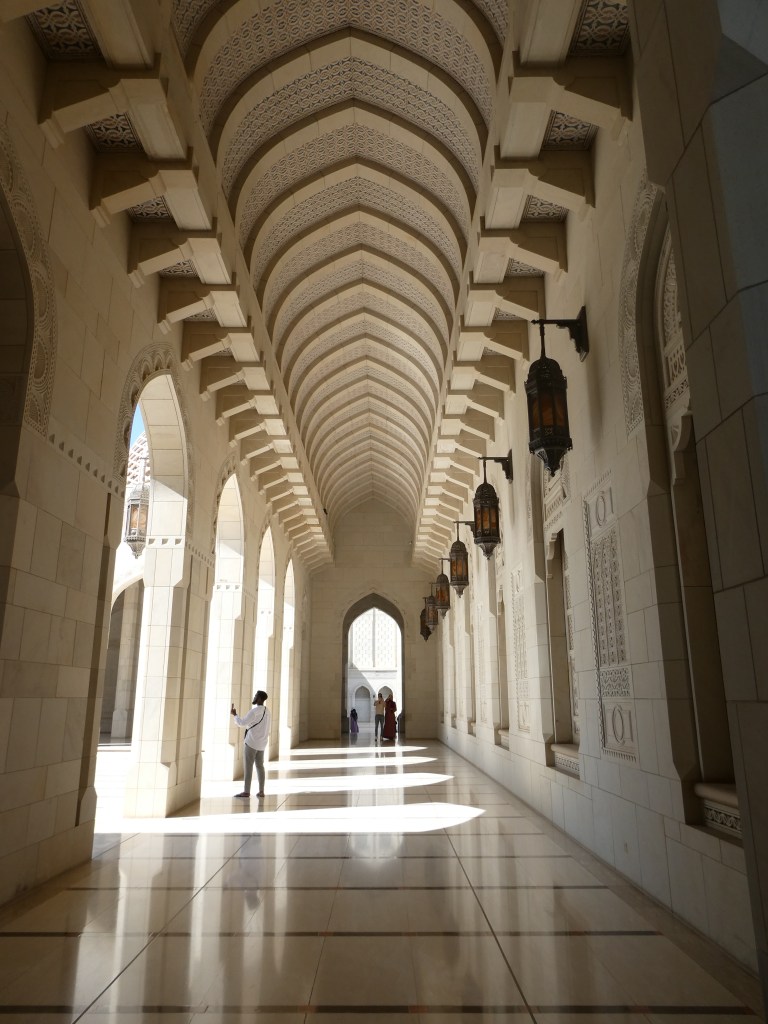 Un long couloir avec des arches décoratives et des lanternes suspendues, baigné de lumière naturelle.