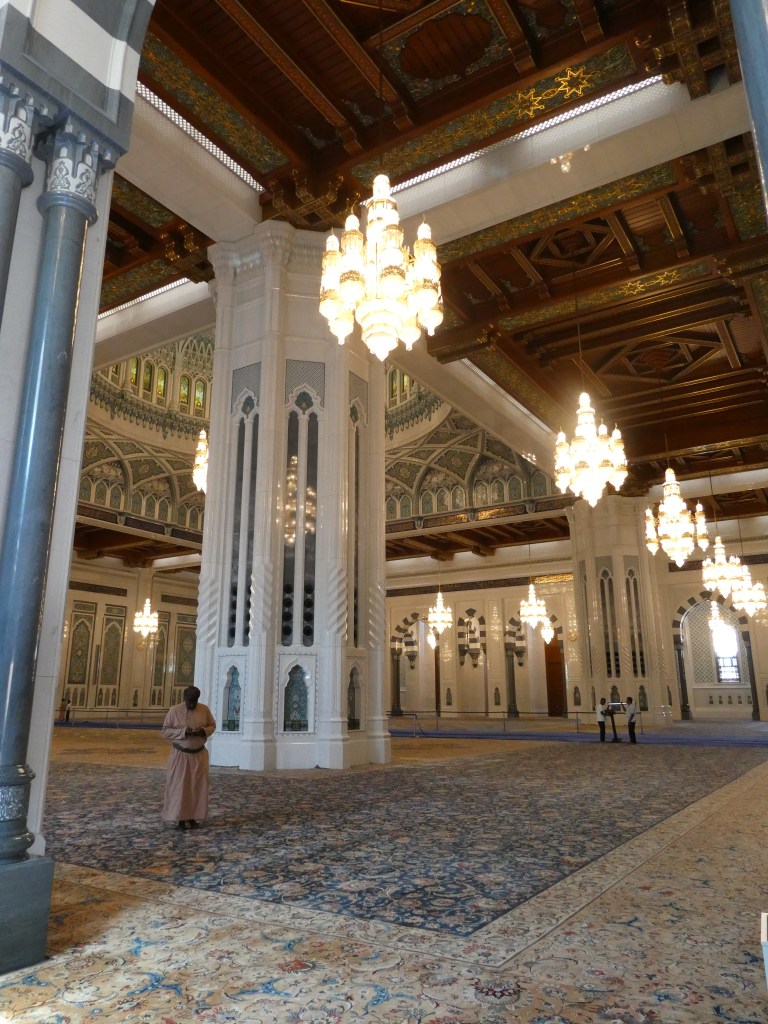 Intérieur d'une mosquée avec des colonnes blanches et des lustres élégants, décorations complexes sur les murs et un sol moquetté.
