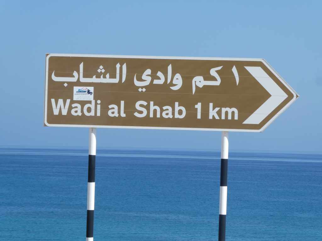 Panneau indiquant Wadi al Shab à 1 km, avec une flèche directionnelle.