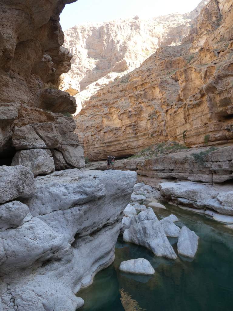 Un canyon avec des falaises rocheuses et un ruisseau turquoise au fond, des randonneurs se tenant sur une falaise.