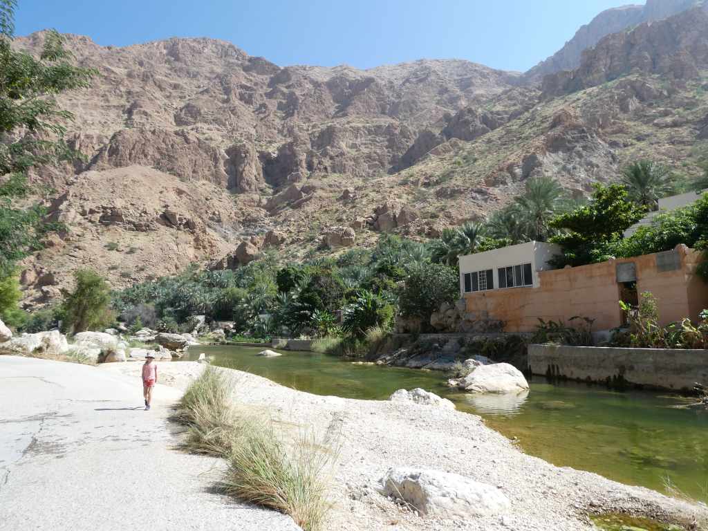 Un enfant marchant le long d'une rivière dans un canyon entouré de collines rocailleuses et de végétation luxuriante.