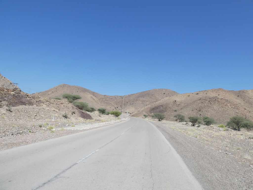 Route sinueuse à travers des collines désertiques sous un ciel bleu.