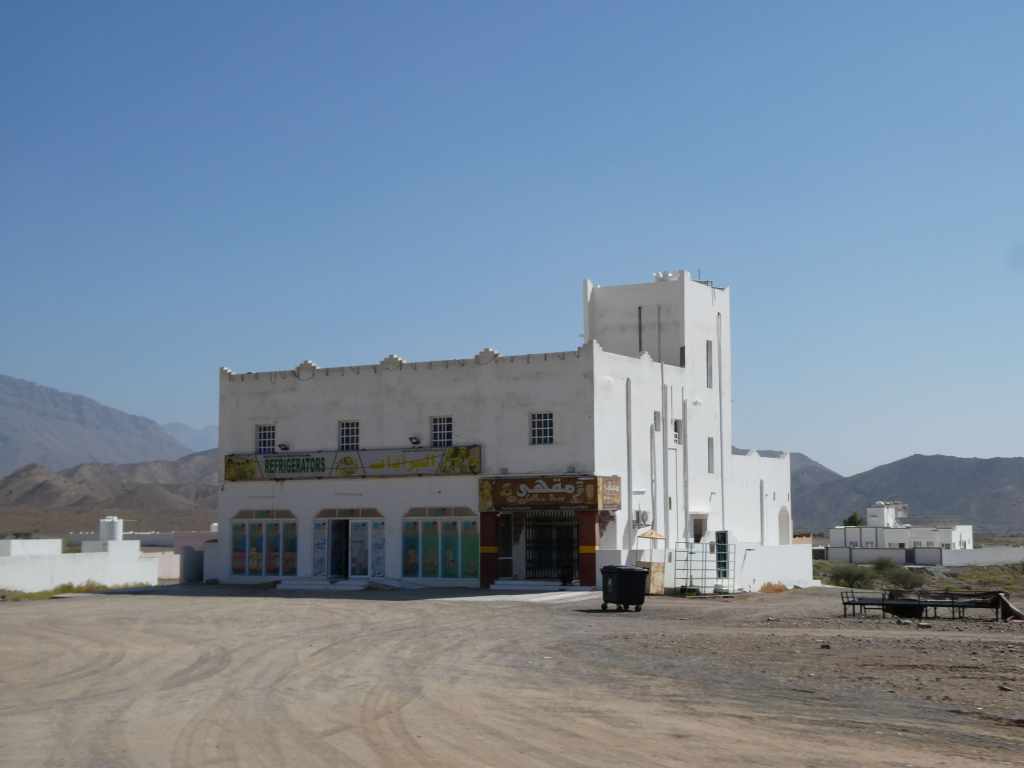 Un bâtiment blanc avec des magasins au milieu d'un paysage désertique, entouré de montagnes.