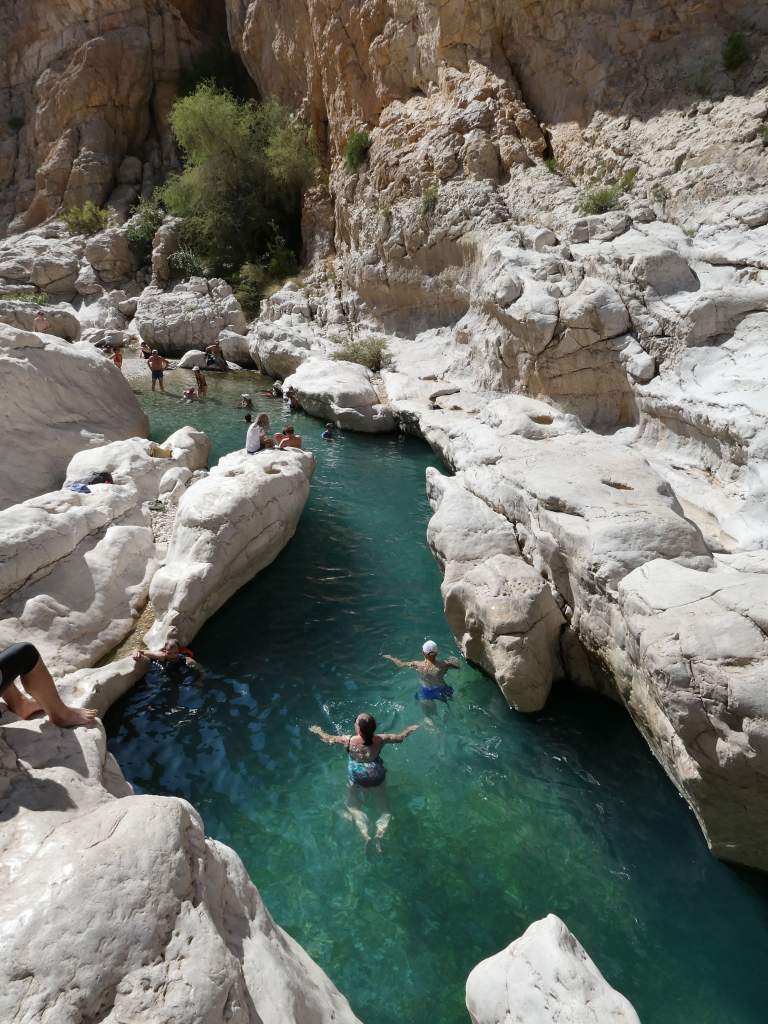 Des personnes se baignent dans une piscine naturelle entourée de rochers dans un canyon.