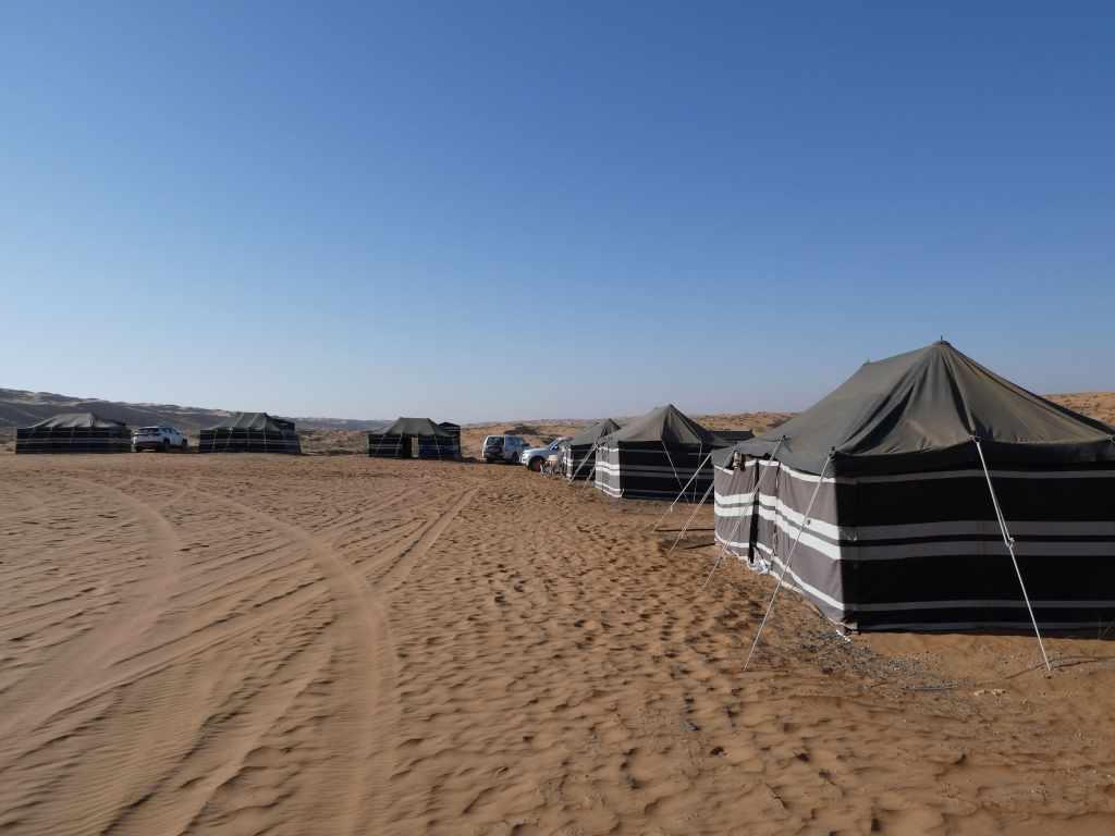 Des tentes de camping dans un désert sous un ciel bleu, avec des véhicules stationnés à proximité.