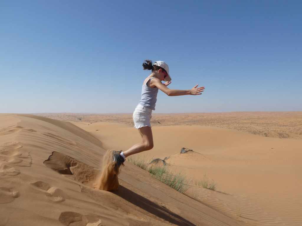 Une fille sautant sur une dune de sable dans le désert, avec un paysage désertique en arrière-plan.