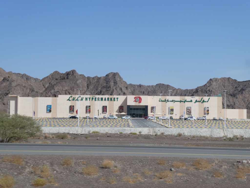 Vue extérieure du hypermarché Lulu, situé devant des montagnes, avec un parking rempli de voitures.