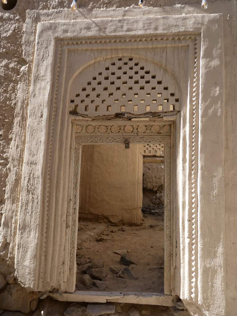 Une porte ornée avec des motifs géométriques et des détails sculptés, menant à l'intérieur d'un bâtiment ancien.