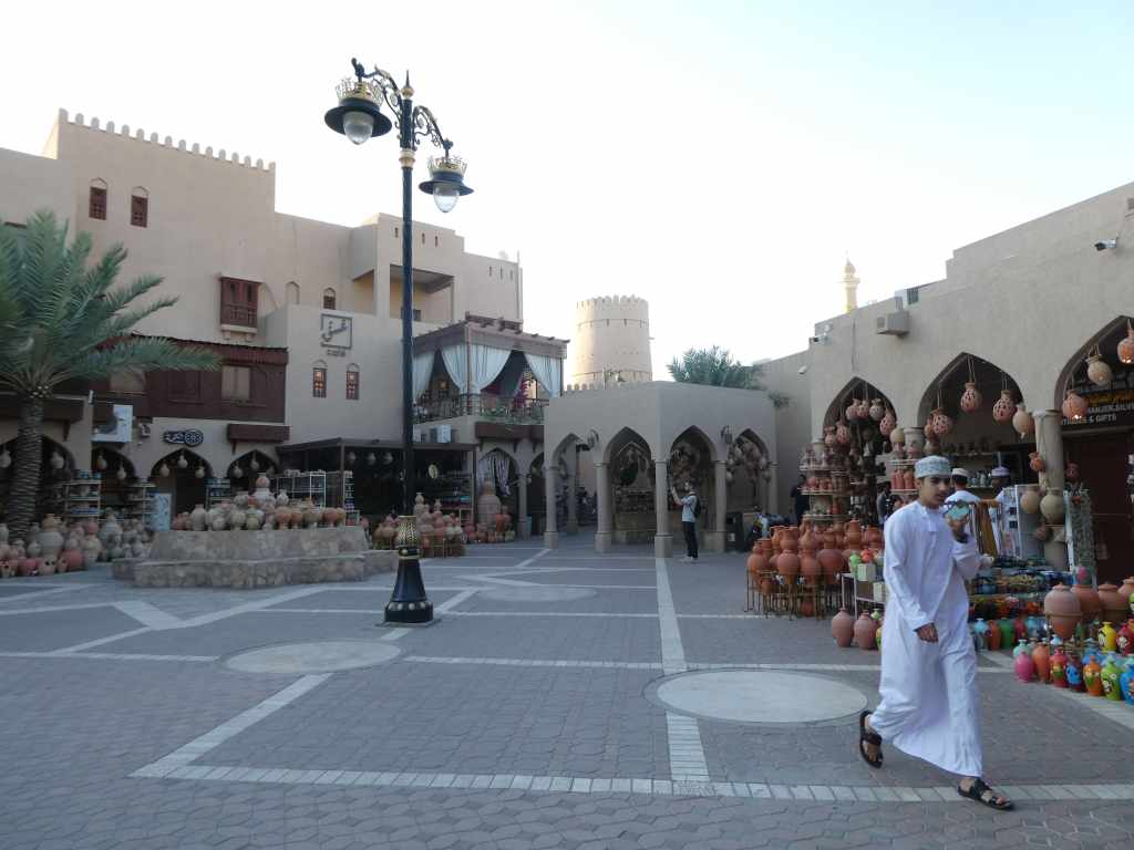 Un marché traditionnel avec des poteries et des objets artisanaux, un homme en tenue traditionnelle marchant sur la place.